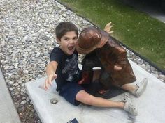 a young boy sitting on the ground next to a statue of a man with his mouth open