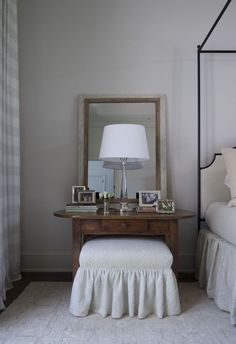 a white bed sitting next to a wooden table with a lamp on top of it