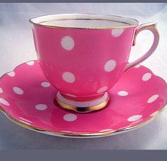 a pink cup and saucer with white polka dots on the rim, sitting on a plate