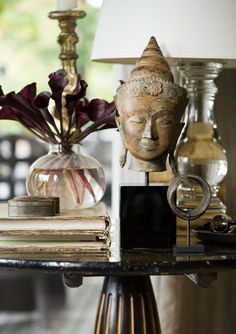 a table topped with a vase filled with flowers and a buddha head next to a lamp