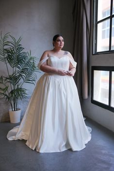 a woman standing in front of a window wearing a white dress and holding her hands on her hips