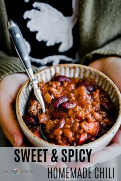 a person holding a bowl of chili with a spoon in it and wearing a sweater