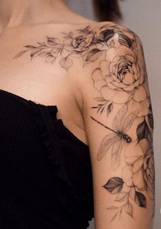 a woman's shoulder with flowers and leaves on her left arm, which is covered in black ink