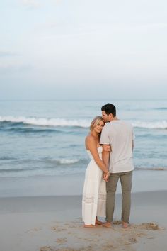 a man and woman standing on top of a sandy beach next to the ocean holding hands