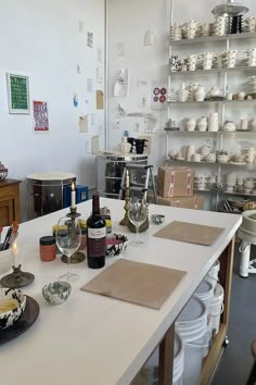 a table with plates and wine glasses on it in a room filled with shelves full of dishes