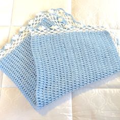 two blue crocheted bags sitting on top of a white tablecloth covered floor