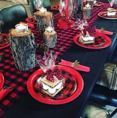 the table is set with red and black place mats, plaid napkins, silverware, candlesticks, and glass vases