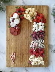 a wooden cutting board topped with fruit and veggies next to candy canes