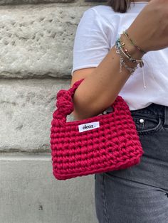 a woman is holding a red crocheted handbag in her right hand and she is wearing a white t - shirt