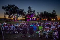 an outdoor concert with people sitting in lawn chairs watching the sun go down at night