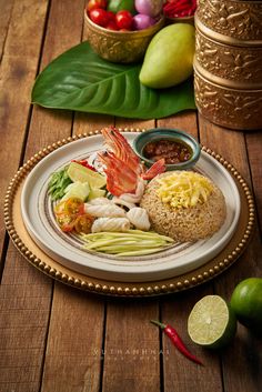 a white plate topped with lots of food on top of a wooden table next to fruit and vegetables