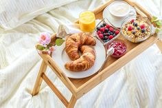 a tray with breakfast foods and drinks on it, including croissants, berries, orange juice, yogurt