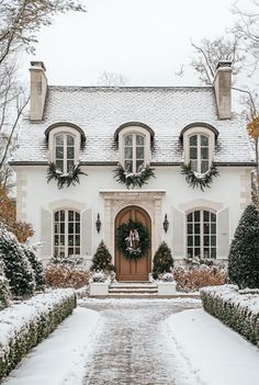 a house covered in snow with wreaths on the front door and two windows above it