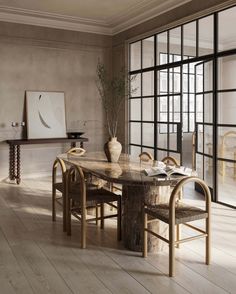 a dining room table with chairs and a vase on the table in front of large windows