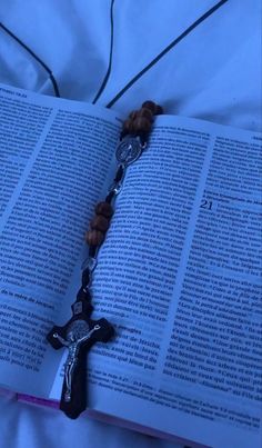 an open book with a rosary on it laying on top of a bed next to a cross