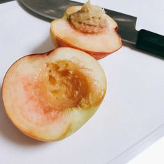 two pieces of peach sitting on top of a cutting board with a knife next to it