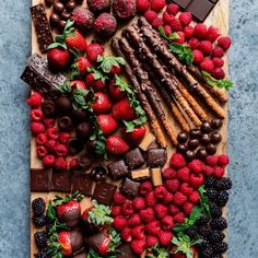 an assortment of chocolates, strawberries and berries on a cutting board with mint leaves