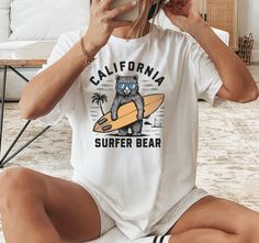 Embrace the laid-back beach vibes with our California Surfer Bear T-Shirt. Featuring an adorable bear ready to catch some waves with his surfboard, this tee is perfect for summer outings, beach trips, or casual wear. Let's add a bit of fun and adventure to your wardrobe with this unique, eye-catching design. Grab yours now and show off your love for surfing and beach life. At BOP Prints, we believe in delivering both style and comfort with every design 👕✨. Our shirts are crafted using the high-quality Bella + Canvas 3001 tees, known for their superior softness, lightweight feel, and long-lasting durability 🧵👌. Whether you're looking for the perfect gift 🎁 or something unique for yourself, our shirts are designed with care to provide a great fit and a fantastic look.  Have questions or Bear Graphic Tee, California Surfer, Summer Surf, Surf Tshirt, Beach Trips, Bear Graphic, Bear Shirt, Bear T Shirt, Beach Vibes