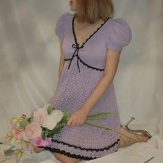 a woman sitting on the floor with flowers in her hand and wearing a purple dress