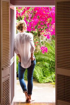 a woman standing in an open doorway with her back to the camera and looking at pink flowers