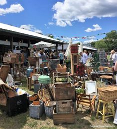 an outdoor flea market filled with lots of furniture and people standing around it on the grass