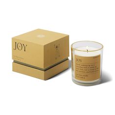 a candle that is next to a box on a white surface with the word joy written in it