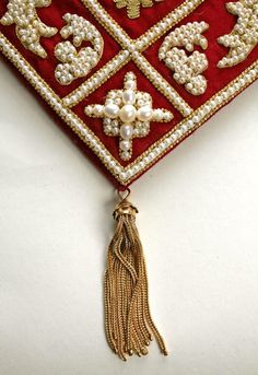 a red and gold brooch with pearls hanging from it's side on a white surface