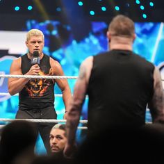 a man holding a microphone standing next to a wrestling ring