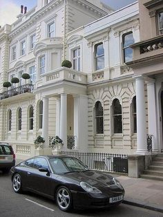 a black car is parked in front of a white building with many windows and balconies