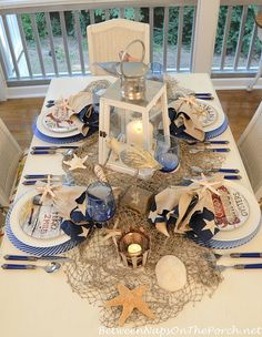 the table is set with blue and white plates, napkins, and seashells