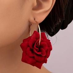 a woman wearing large gold hoop earrings with a red flower on the end of it