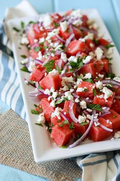 watermelon salad with feta cheese and onions on a white plate next to a blue striped napkin