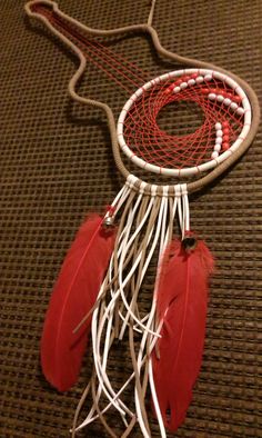 a red and white dream catcher with feathers on it's back end, sitting on a brown carpet