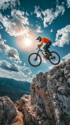 a man on a mountain bike jumping over the top of a cliff in the sun