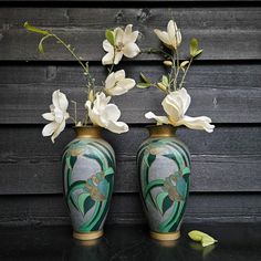 two vases with flowers in them sitting on a table next to a wooden wall