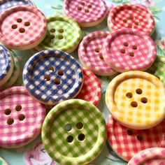 many different colored buttons on a blue and green table cloth with flowers in the background