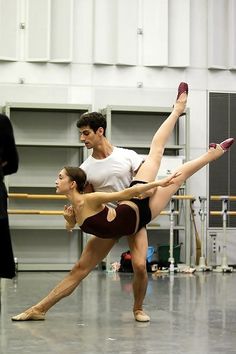 two ballet dancers are performing in a dance studio with one holding the other's leg