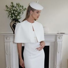 a woman standing in front of a fireplace wearing a white dress with a veil on it