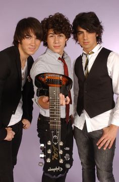 three young men posing for a photo with an electric guitar in front of purple background