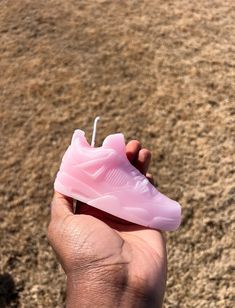 a person holding a pink shoe in their hand on the ground with dirt and grass behind them