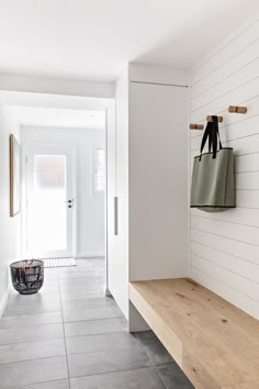 a white hallway with a wooden bench and two bags hanging on the wall next to it