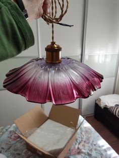 a person holding a pink and purple lamp in front of a box on a bed