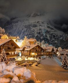 a snow covered mountain with houses in the foreground and lights on at night time