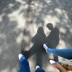 two people standing next to each other in the street with their shadows on the ground