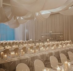 a banquet hall with tables and chairs covered in white draping, lit by candles