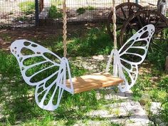 a white butterfly shaped swing hanging from a rope next to a wooden bench in the grass