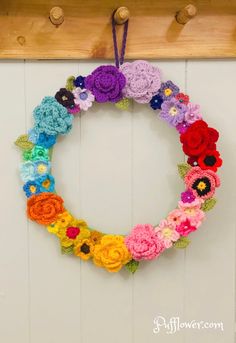 a colorful crocheted wreath hanging on the wall with flowers around it and text overlay that says, free crochet pattern