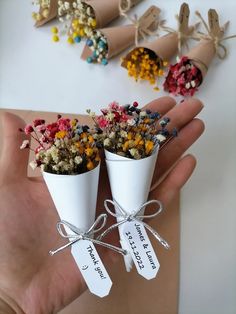 two small white vases filled with flowers on top of a table next to tags