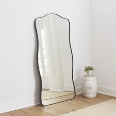 a mirror sitting on top of a wooden floor next to a vase