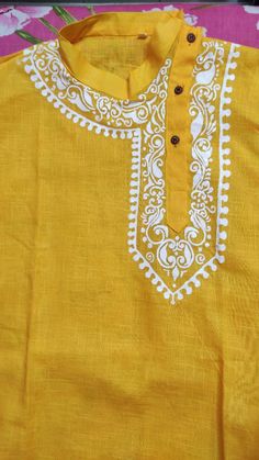 an embroidered yellow shirt with white trims and buttons on the collar, sitting on a bed